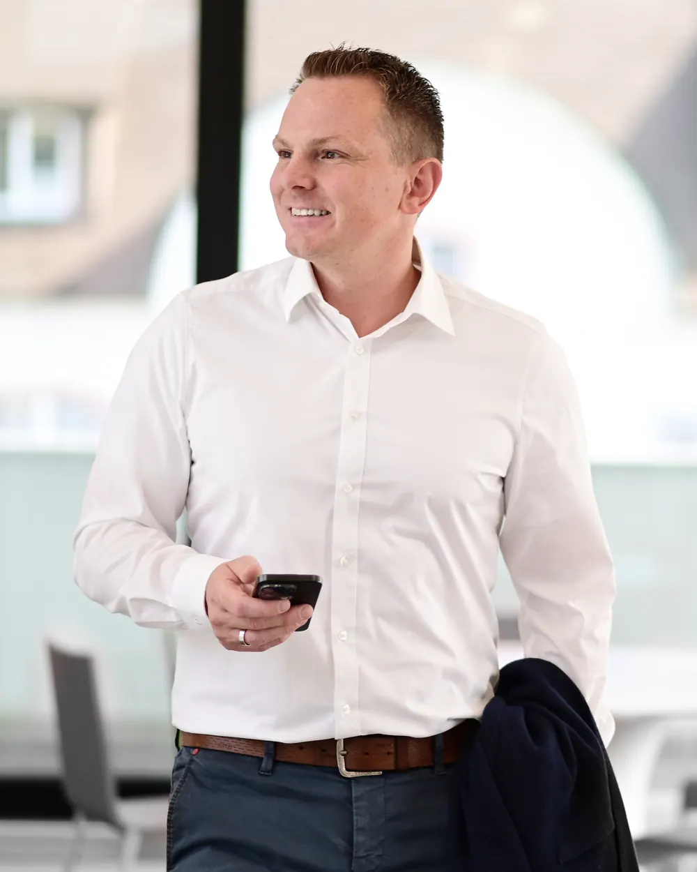 Steuerberater Dominic Molz am Fenster, mit dem Smartphone in der Hand